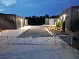 Gated entrance at dusk with pole lights along the drive aisle between two buildings